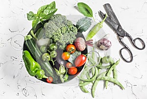 Fresh vegetables - broccoli, zucchini, beets, peppers, tomatoes, green beans, garlic, basil in a metal basket on a light