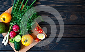 Fresh vegetables on a cutting board with herbs for salad on a dark background. Diet food top view with place for text