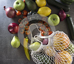 Fresh vegetables and fruits in white cotton mesh bag. Gray background. Healthy eating concept.