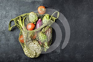 Fresh vegetables in a green string bag on a black background. Cauliflower, tomatoes, artichokes, asparagus and zucchini