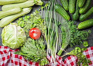 Fresh vegetables and greens in bunches arranged in a frame on a black stone background.