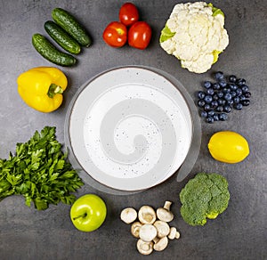 Fresh vegetables and herbs around a round empty plate on a table top view. The concept of healthy eating.