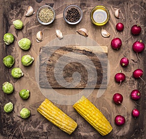 Fresh vegetables ingredients radishes, brussels sprouts, corn, seasoning lined around the cutting board wooden rustic backgroun