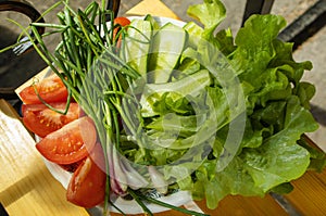 Fresh vegetables - lettuce, green onion, tomatoes and cucumbers on a white plate on a wooden background. The concept of