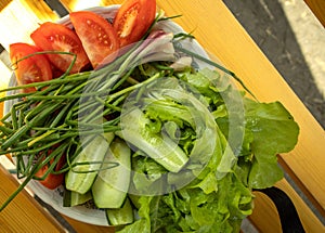 Fresh vegetables - lettuce, green onion, tomatoes and cucumbers on a white plate on a wooden background. The concept of