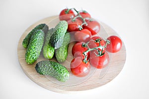 Fresh vegetables lie on a white background wooden cutting board, top view. Tomatoes on a branch, cucumbers gherkins.