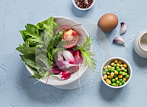 Fresh vegetables - radishes, tomatoes, garden herbs, green peas, chickpeas and egg on a light blue stone background.