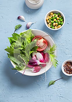 Fresh vegetables - radishes, tomatoes, garden herbs and green peas and chickpeas on a light blue stone background.