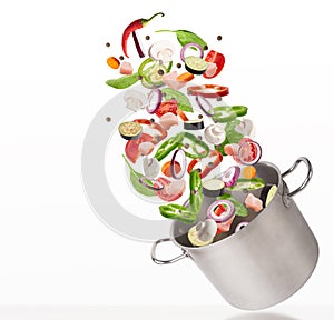 Fresh vegetables and raw meat flying into steel stewpot