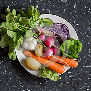 Fresh vegetables - red cabbage, radishes, carrots, potatoes, garlic, onions on a dark stone background. Healthy vegetarian, diet,