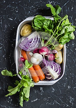 Fresh vegetables - red cabbage, radishes, carrots, potatoes, garlic, onions on a dark stone background. Healthy vegetarian, diet,
