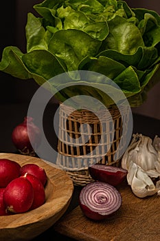 Fresh vegetables - salad, radish, onions and garlic lie on a wooden board and bowl