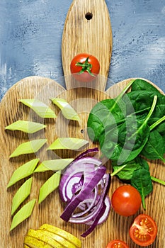 Fresh vegetables are sliced on a cutting board, cherry tomatoes, spinach, cabbage, celery. Vegetarian dinner. Top view.