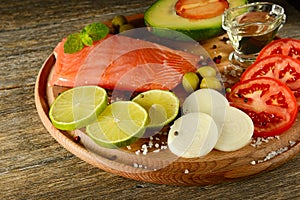 Fresh vegetables and smoked fish on wooden board in rustic kitchen. Salmon, lime, onions, olives, tomatoes and olive oil.