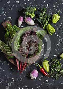 Fresh vegetables - swiss chard, broccoli, pepper, turnip. On a dark background, top view.