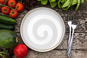 Fresh vegetables for tasty vegan and diet cooking or salad making around empty plate on rustic wooden background, top view.