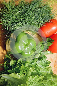 Fresh vegetables, tomato, lettuce, dill, parsley, bell pepper lie on a wooden table.