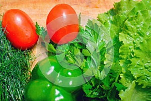 Fresh vegetables, tomato, lettuce, dill, parsley, bell pepper lie on a wooden table.