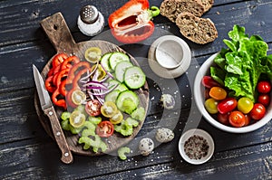 Fresh vegetables - tomatoes, cucumbers, peppers, celery and garden herbs and spices on dark wooden background.