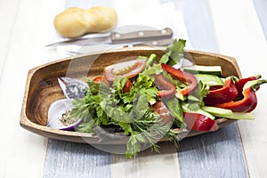 Fresh vegetables on a wooden plate with fork and knife. Red pepper, tomato, cucumber, radish, parsley, dill healthy diet.