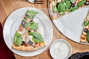 Fresh vegetarian pizza with spinach, black olives and almonds on wooden table in restaurant.