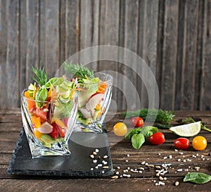 Fresh vegetarian salad in glasses served on slate board with ingredients around, top view