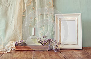 Fresh vintage perfume bottle next to aromatic flowers and antique blank frame on wooden table. retro filtered image