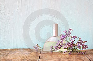 Fresh vintage perfume bottle next to aromatic flowers on wooden table. retro filtered image