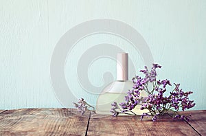 Fresh vintage perfume bottle next to aromatic flowers on wooden table. retro filtered image