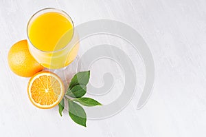 Fresh vitamin summer yellow beverage of ripe oranges with green leaf on light white wood background, top view, border.