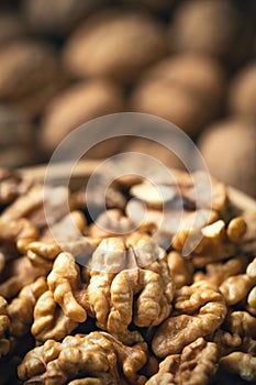 Fresh walnut kernels in a bowl and blurred whole walnuts in background.