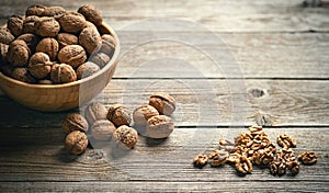 Fresh walnut kernels and whole walnuts in a bowl on rustic old wooden table.
