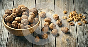 Fresh walnut kernels and whole walnuts in a bowl on rustic old wooden table.