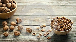 Fresh walnut kernels and whole walnuts in a bowl on rustic old wooden table.