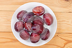 Fresh washed plums on dish on rustic table, top view