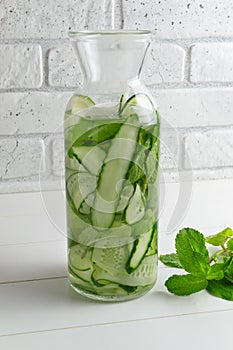 Fresh water infused with cucumbers and mint sprigs, detox drink. Water is poured into the jug. Health care, fitness, healthy food