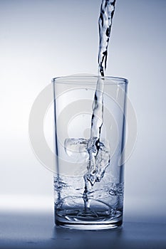 Fresh water poured into glass on blue background