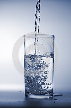 Fresh water poured into glass on blue background