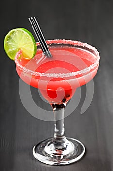 Fresh watermelon cocktail with lime in wineglass on black wooden background