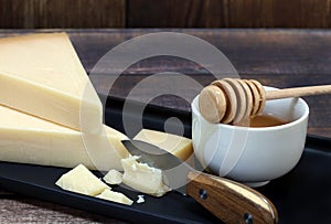 Fresh wedges of Parmesan cheese with a knife and a cut chunk. Bowl of honey to the side