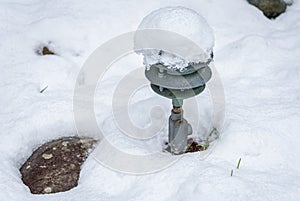 Fresh wet snow covering a garden, old metal light fixture poking out
