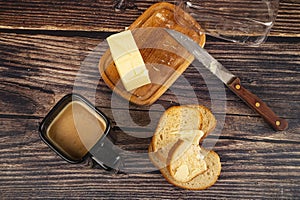 Fresh wheat toast with butter, butter in a wooden butter dish, a knife with a wooden handle and a Cup of coffee with milk on a