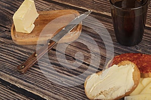 Fresh wheat toast with butter, sausage and cheese, a wooden butter dish with a piece of butter and a mug of tea on a wooden