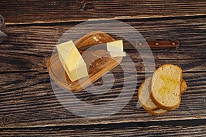 Fresh wheat toast, butter in a wooden butter dish and a knife with a wooden handle on a wooden background. Close up