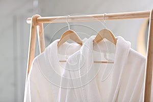 Fresh white bathrobes hanging on rack indoors