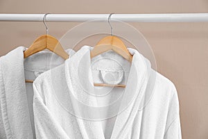 Fresh white bathrobes hanging on rack near beige wall