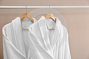 Fresh white bathrobes hanging on rack near wall