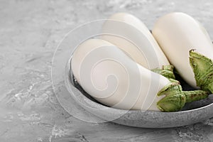 Fresh white eggplants in bowl on grey textured table, closeup. Space for text