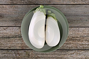 Fresh white eggplants in bowl on wooden table, top view