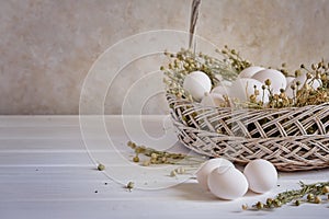 Fresh white eggs in a basket with dried flowers on a white table